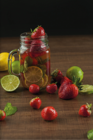 Ein Glas mit fruchtigem Getränk, gefüllt mit Erdbeeren, Limetten und Minze, auf einem Holztisch.